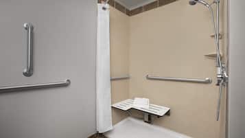 Ein Badezimmer mit Dusche, Haltegriffen, Handtuchhalter und einer Sitzbank.