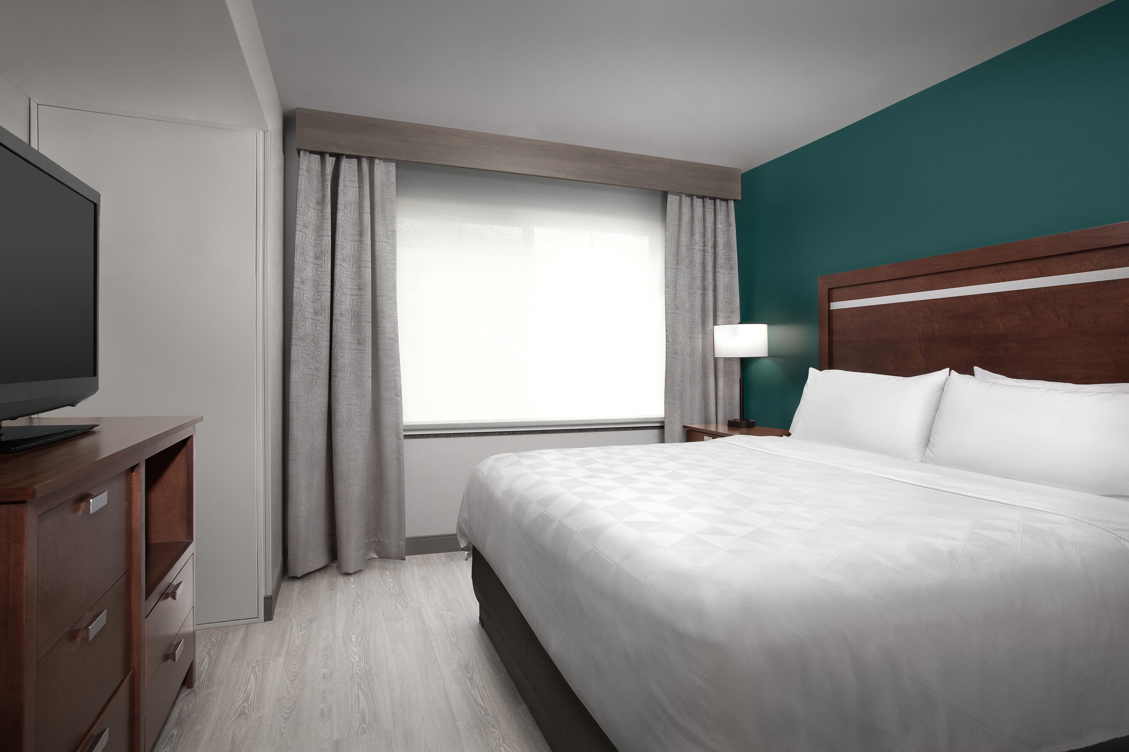 A hotel room with a bed, a TV, a nightstand, and a window with curtains.