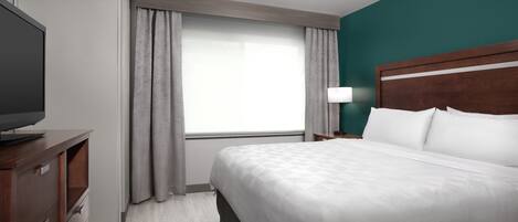 A hotel room with a bed, a TV, a nightstand, and a window with curtains.