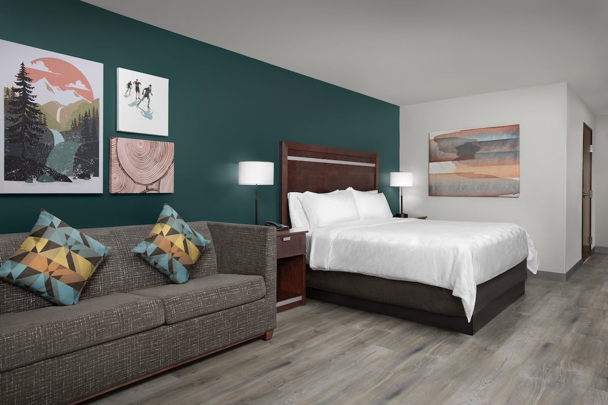 A hotel room with a bed, a sofa, and two wall-mounted lamps.
