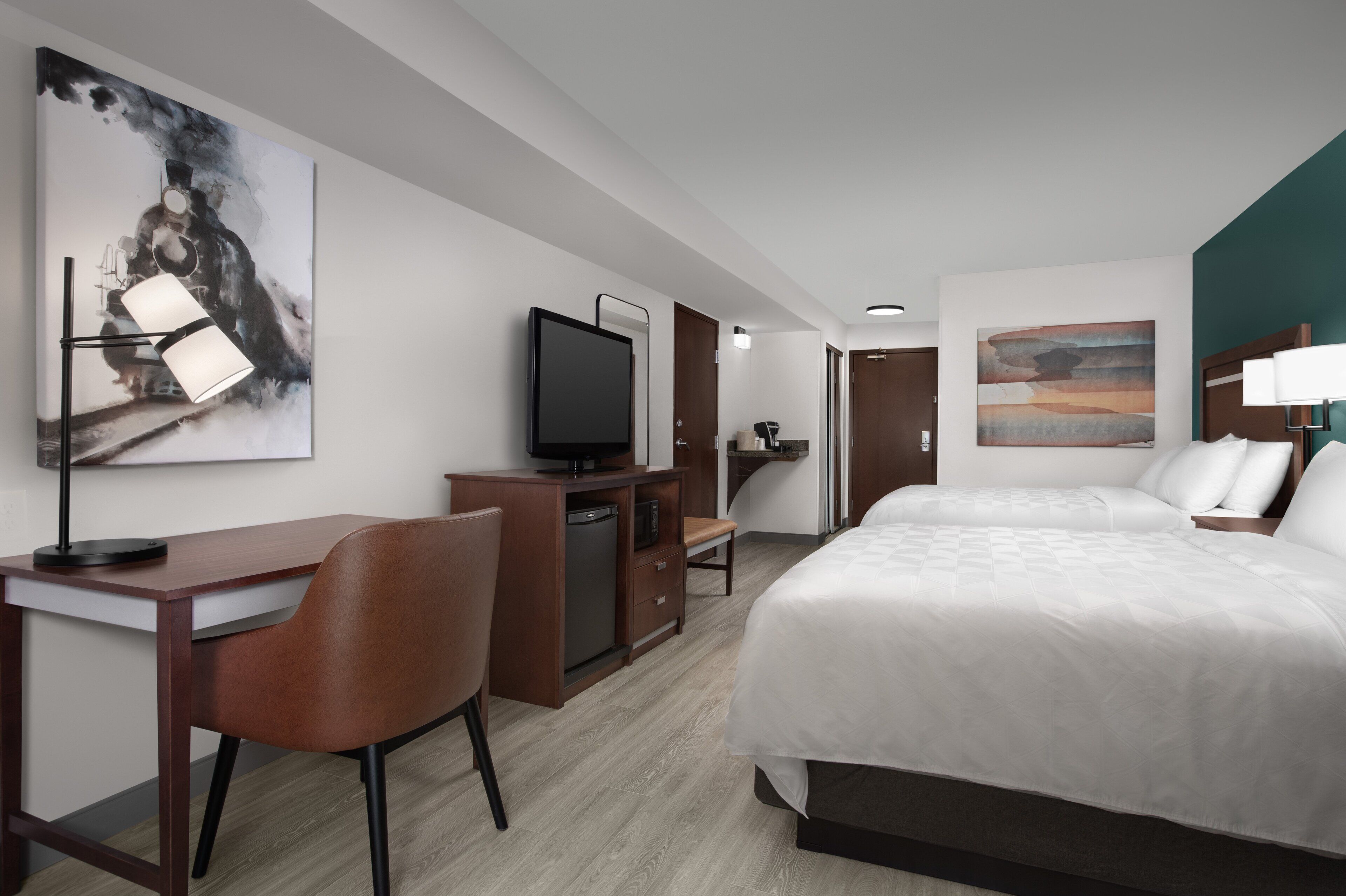 A hotel room with a bed, desk, chair, television, and artwork on the walls.