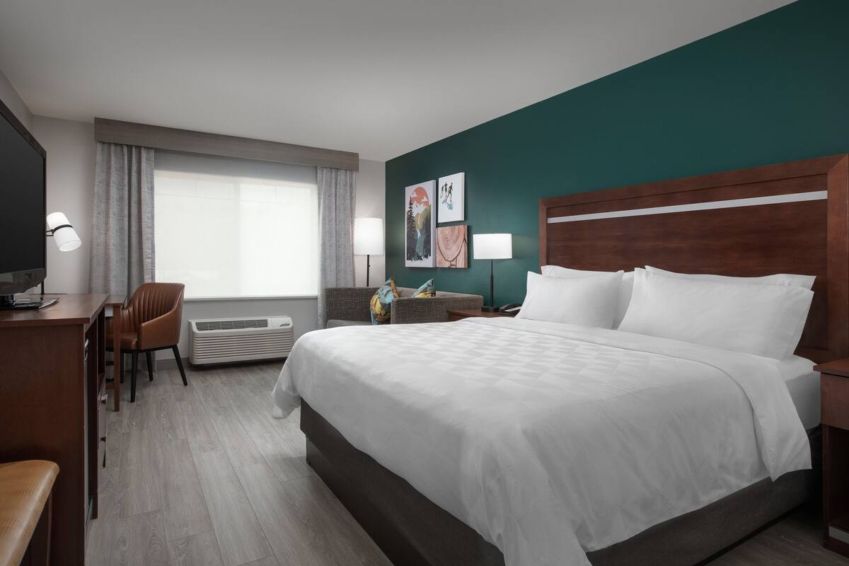 Una habitación de hotel con una cama grande, un escritorio con silla, un televisor y una ventana con cortinas.
