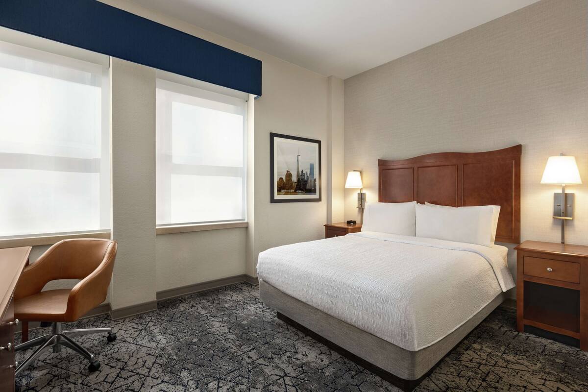 A hotel room with a large bed, a desk, a chair, and two bedside tables with lamps.