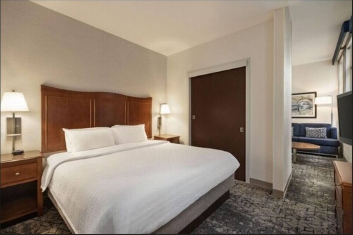 A hotel room with a large bed, wooden headboard, two bedside tables with lamps, a wardrobe, and a sofa in the corner.
