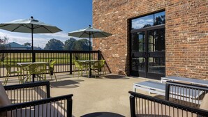 An outdoor patio with tables and chairs, two umbrellas, and a brick building in the background.