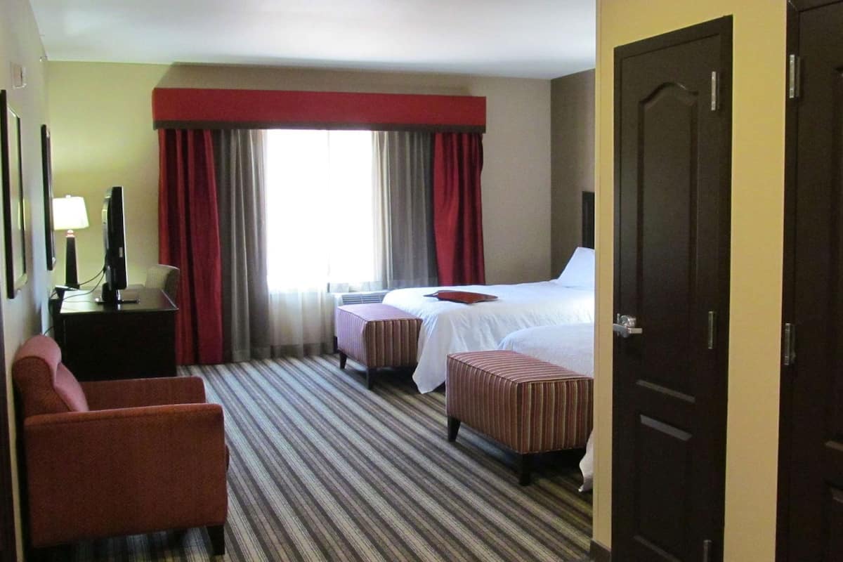 A hotel room with a bed, two bedside tables, a TV, a chair, and a window with curtains.