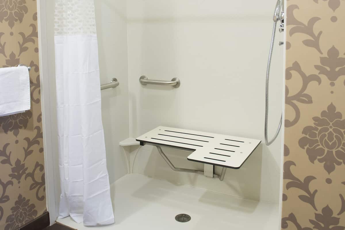 A walk-in shower with a glass door, a white towel hanging on the door, and a showerhead mounted on the wall.