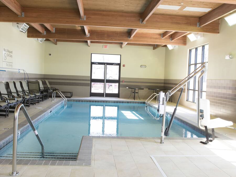 Una piscina interior con vigas de madera, suelo de baldosas y una silla para socorrista.