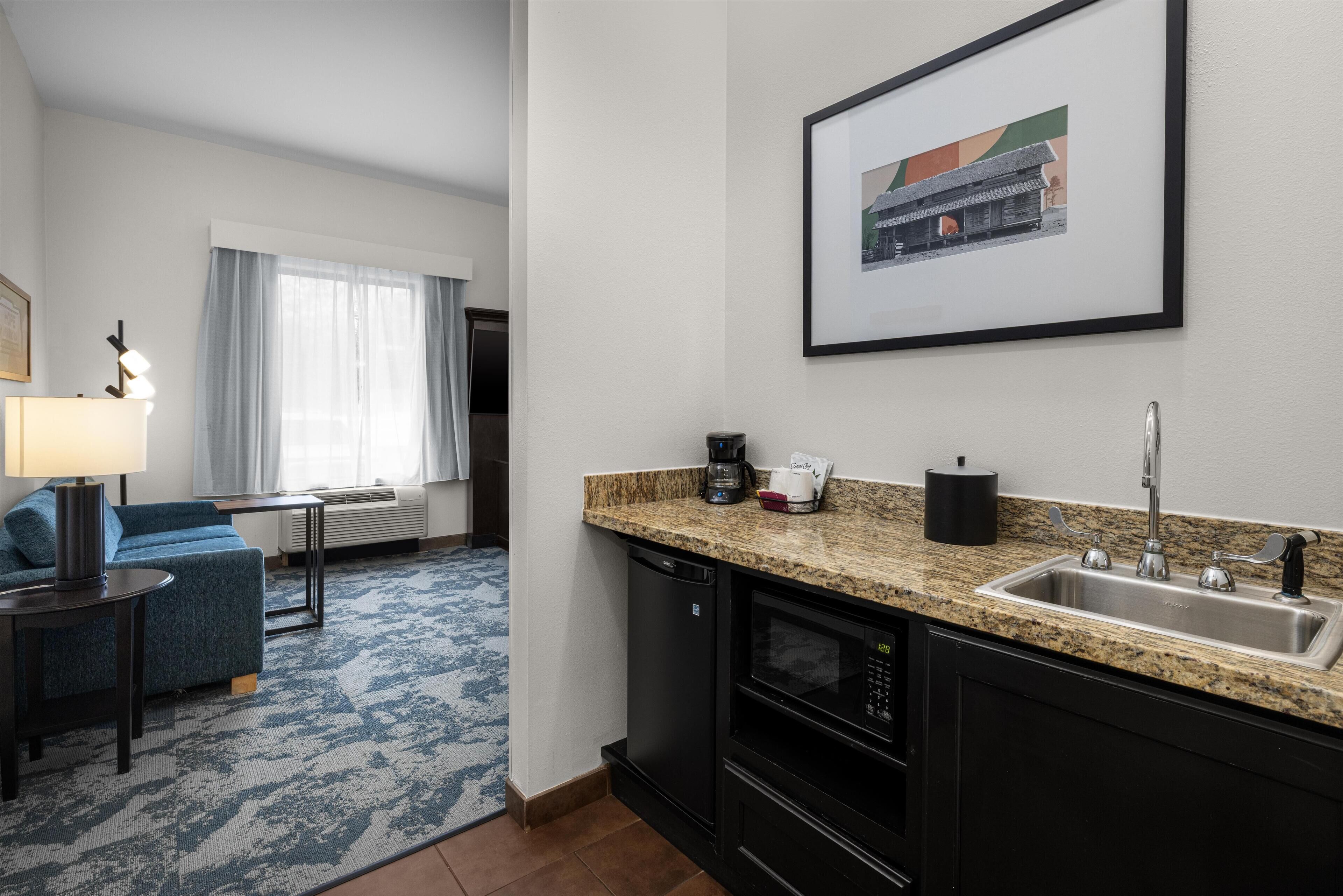 A hotel room with a kitchenette, a dining area with a blue sofa, a coffee maker, and a framed picture on the wall.