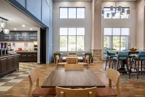 A spacious dining area with a high ceiling, large windows, and a modern kitchen in the background.