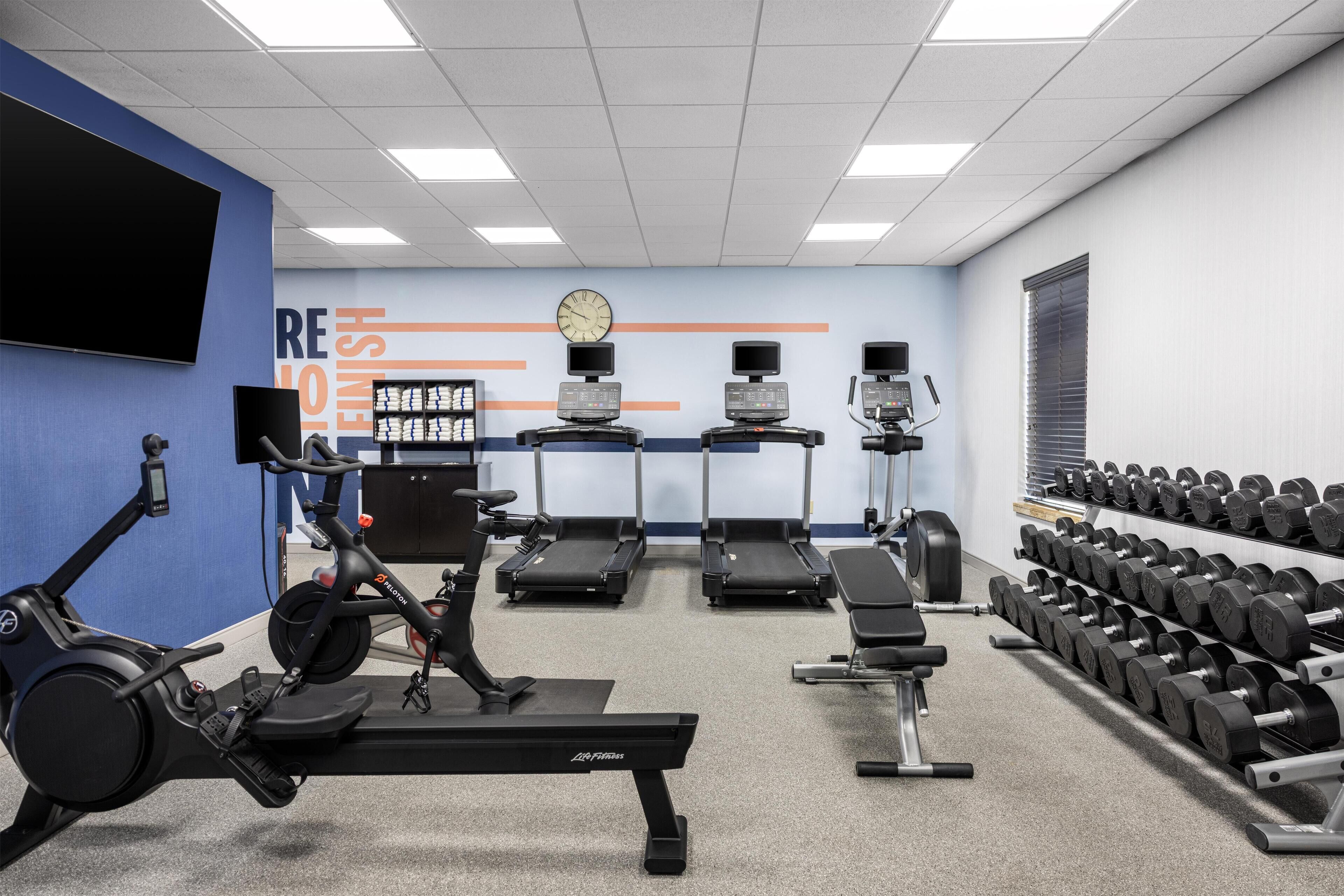 A gym with exercise equipment, a wall clock, and a row of dumbbells.