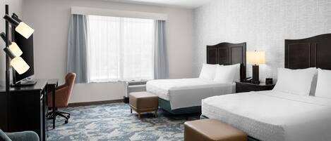 Une chambre d’hôtel avec deux lits, un bureau avec une chaise, une télévision et une fenêtre avec des rideaux.