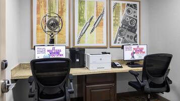 Um espaço de trabalho com duas cadeiras de escritório, uma mesa, dois monitores, uma impressora e quadros na parede.