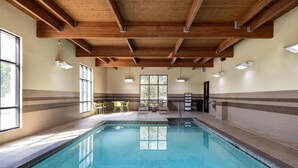 An indoor swimming pool with wooden beams, tiled walls, and seating areas.