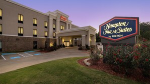 A Hampton Inn & Suites by Hilton building with a sign, parking lot, and landscaped area.