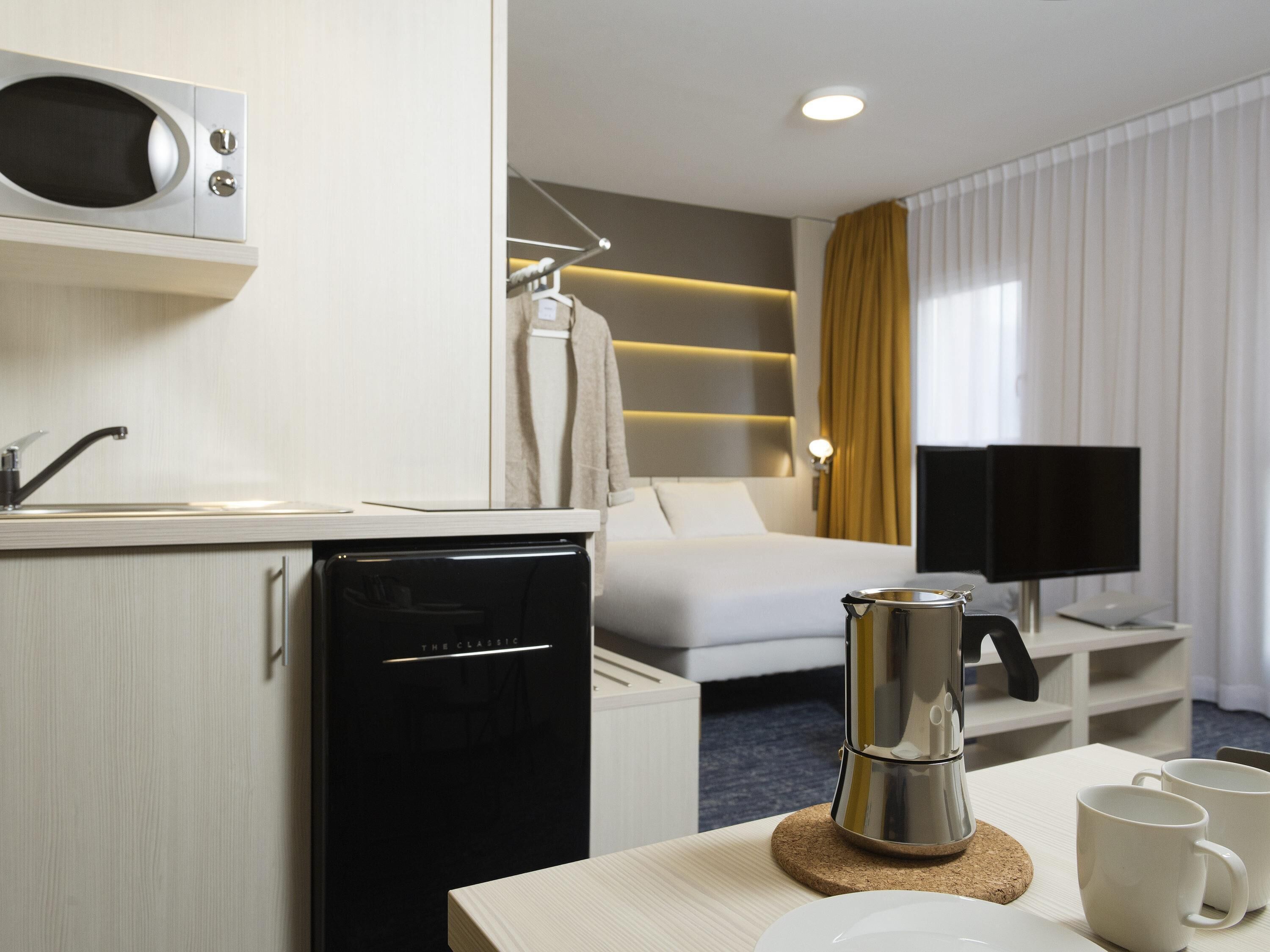 Quarto de hotel com cozinha compacta, cama, televisão e máquina de café.