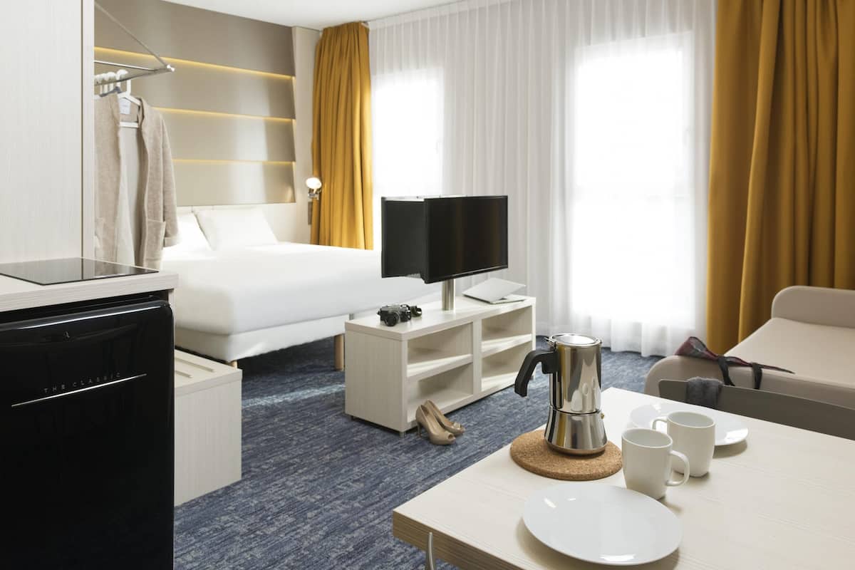 A hotel room with a bed, a TV, a coffee maker, a desk, and a chair.