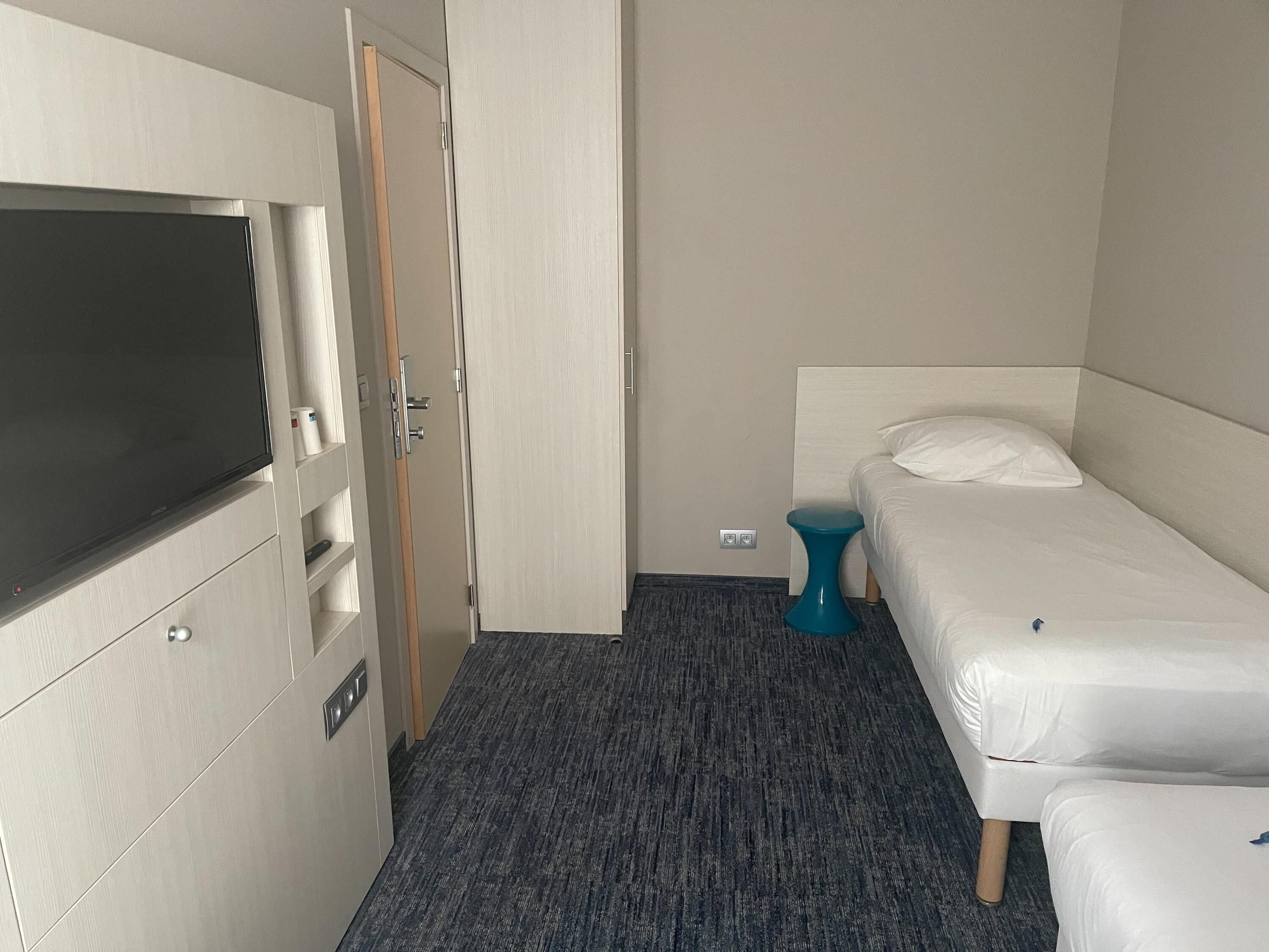 Una habitación de hotel con una cama, una mesita pequeña, un armario y un televisor.