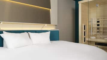 Habitación de hotel moderna con una cama grande, cabecera con iluminación integrada y zona de ducha con paredes de vidrio.