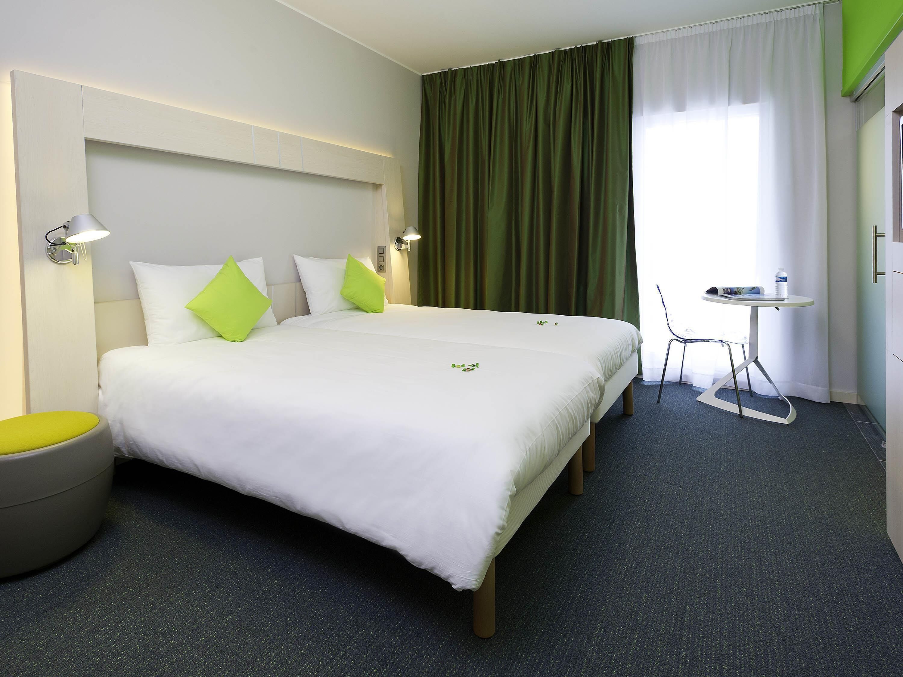 Ein Hotelzimmer mit einem großen Bett, einem kleinen runden Tisch, einem Stuhl und einer Wandleuchte.