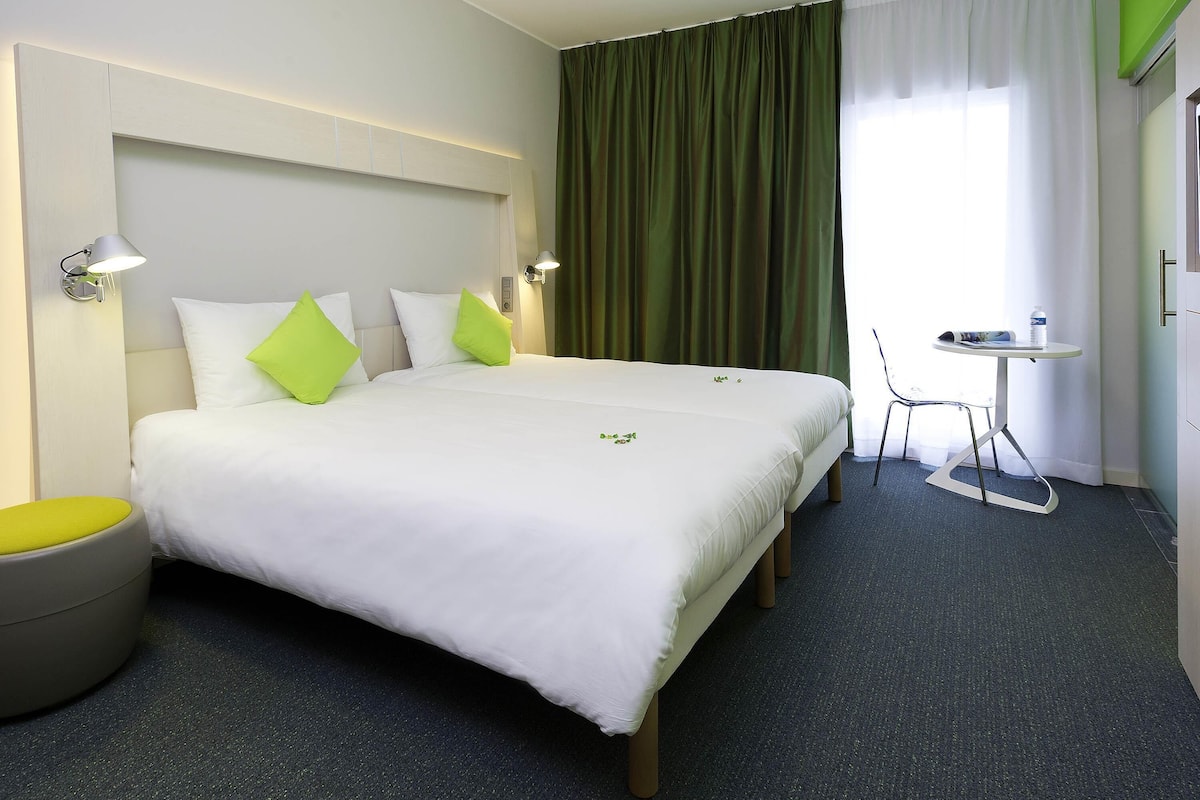 Ein Hotelzimmer mit einem großen Bett, einem kleinen runden Tisch, einem Stuhl und einer Wandleuchte.
