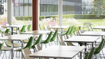 A restaurant with multiple tables and chairs, large windows, and a view of greenery outside.