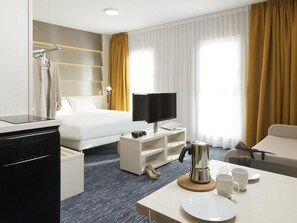 Quarto de hotel com cama, televisão, máquina de café, secretária e cadeira.