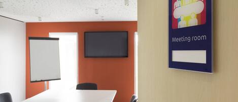 A meeting room with a whiteboard, a flat-screen TV, and a sign indicating the room's purpose.