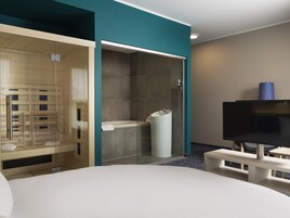 Habitación de hotel moderna con ducha envuelta en vidrio, bañera, televisor de pantalla plana y banco de madera.