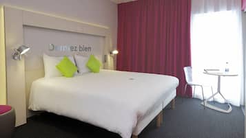 Habitación de hotel con cama, escritorio, silla y ventana con cortinas.