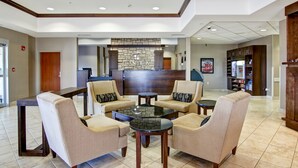 A lobby with a reception desk, seating area with armchairs and a coffee table, and a kitchenette in the background.