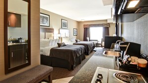 A hotel room with two beds, a kitchenette, a large mirror, and a seating area.