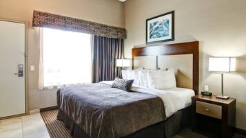 A hotel room with a large bed, a nightstand with a lamp, a window with curtains, and a painting on the wall.