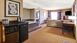 A hotel room with a kitchenette, a sofa, a desk, a flat-screen TV, and a large framed picture on the wall.