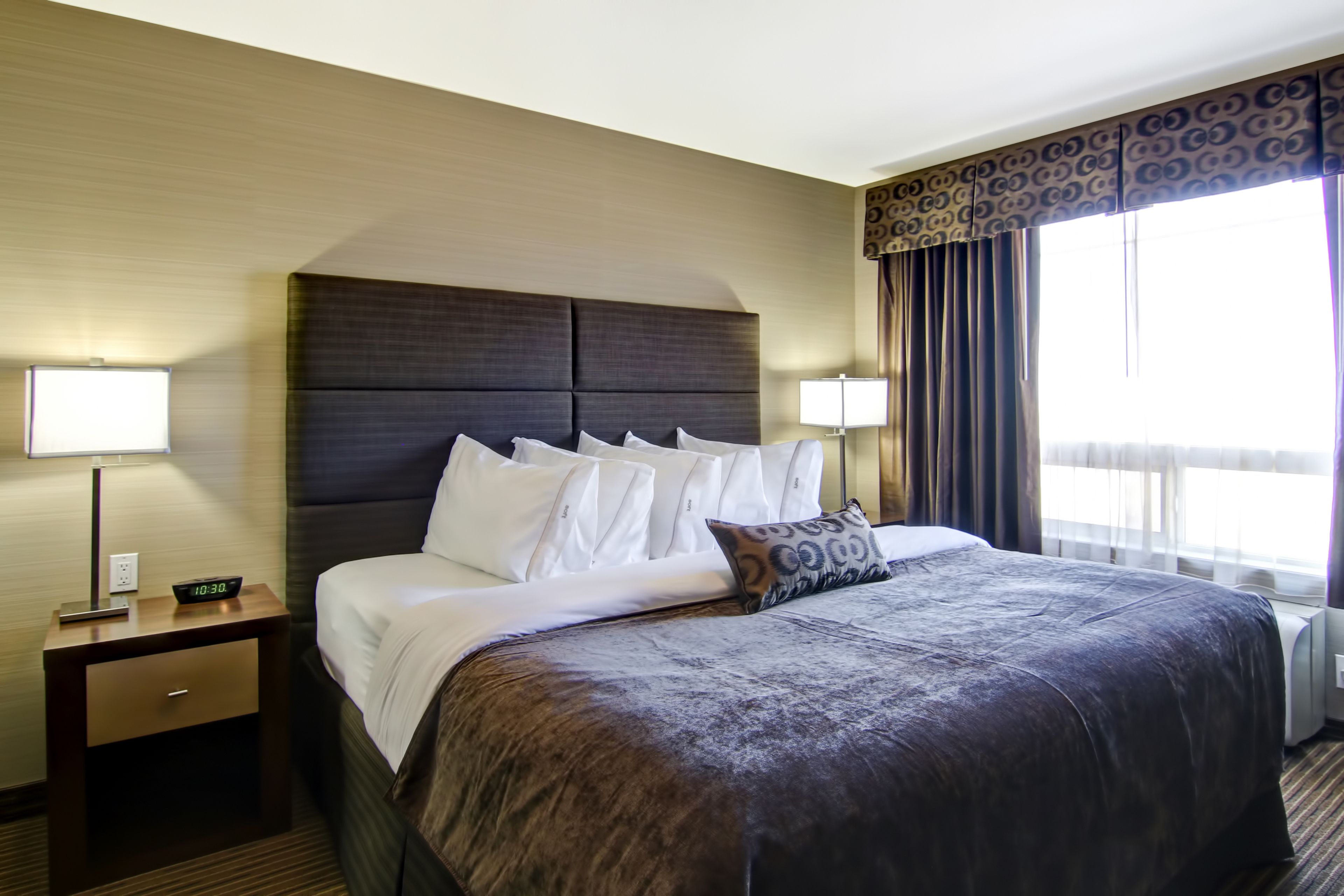 A hotel room with a large bed, two bedside tables, a nightstand, and a window with curtains.