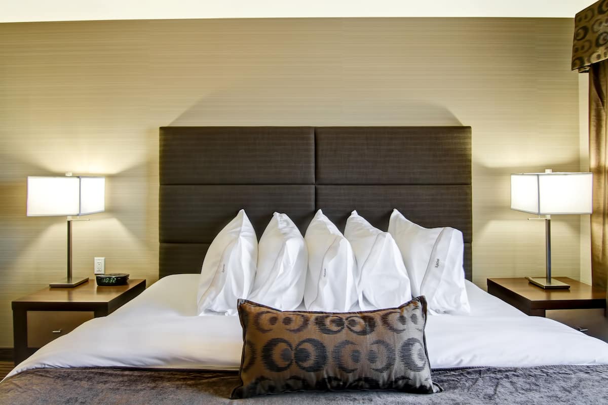 Una habitación de hotel con una cama grande, dos mesitas de noche con lámparas y un cabecero con varios almohadones.