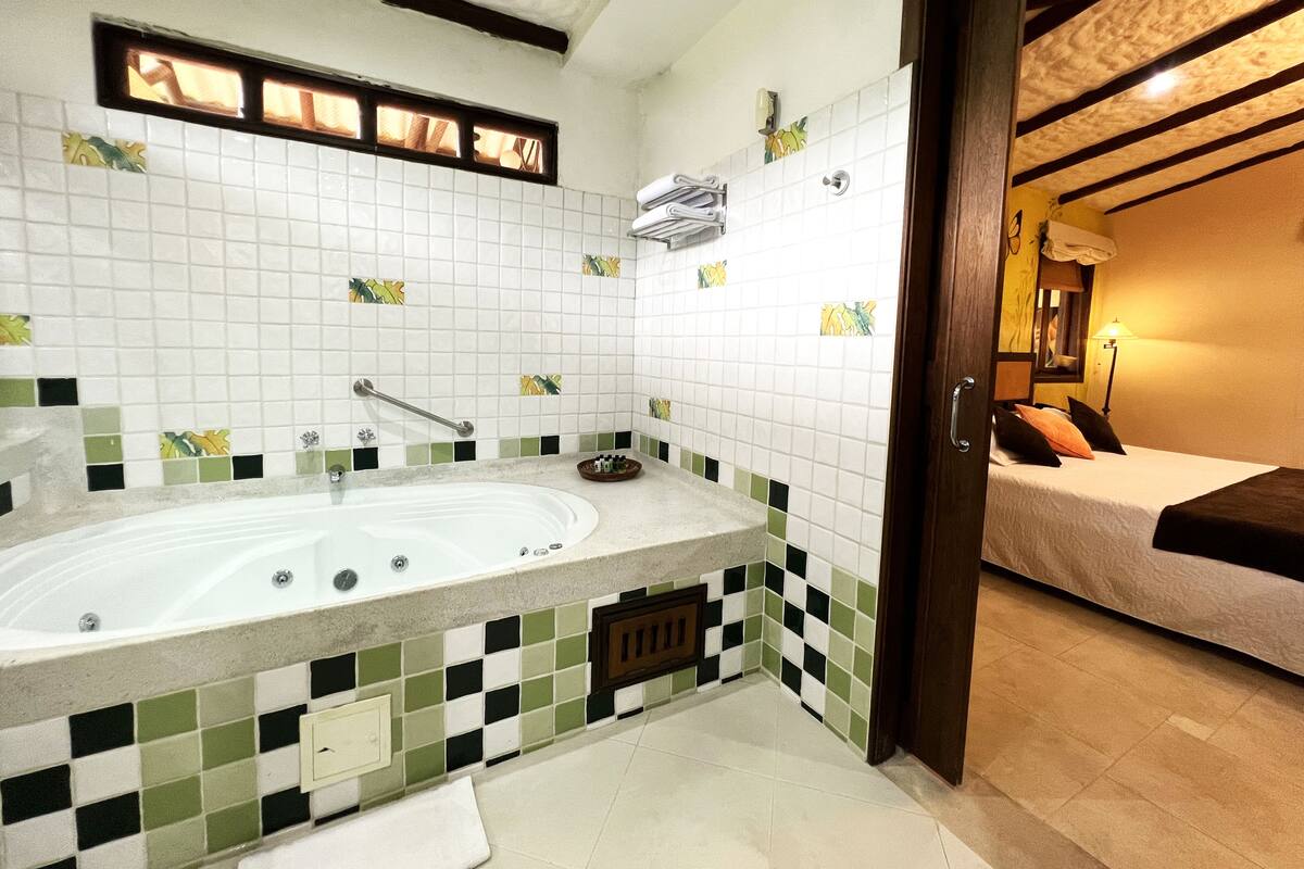 A bathroom with a large bathtub, a shower, and a toilet. There is a window with curtains and a towel rack above the bathtub.