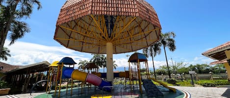 Un parque infantil con una gran estructura tipo sombrilla, toboganes y una zona de juegos circular.