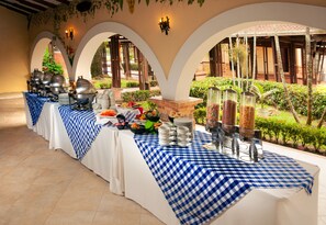 A buffet setup with a checkered tablecloth, food items, and a garden view. - Tequendama Hotel Campestre Villavicencio (Villavicencio)