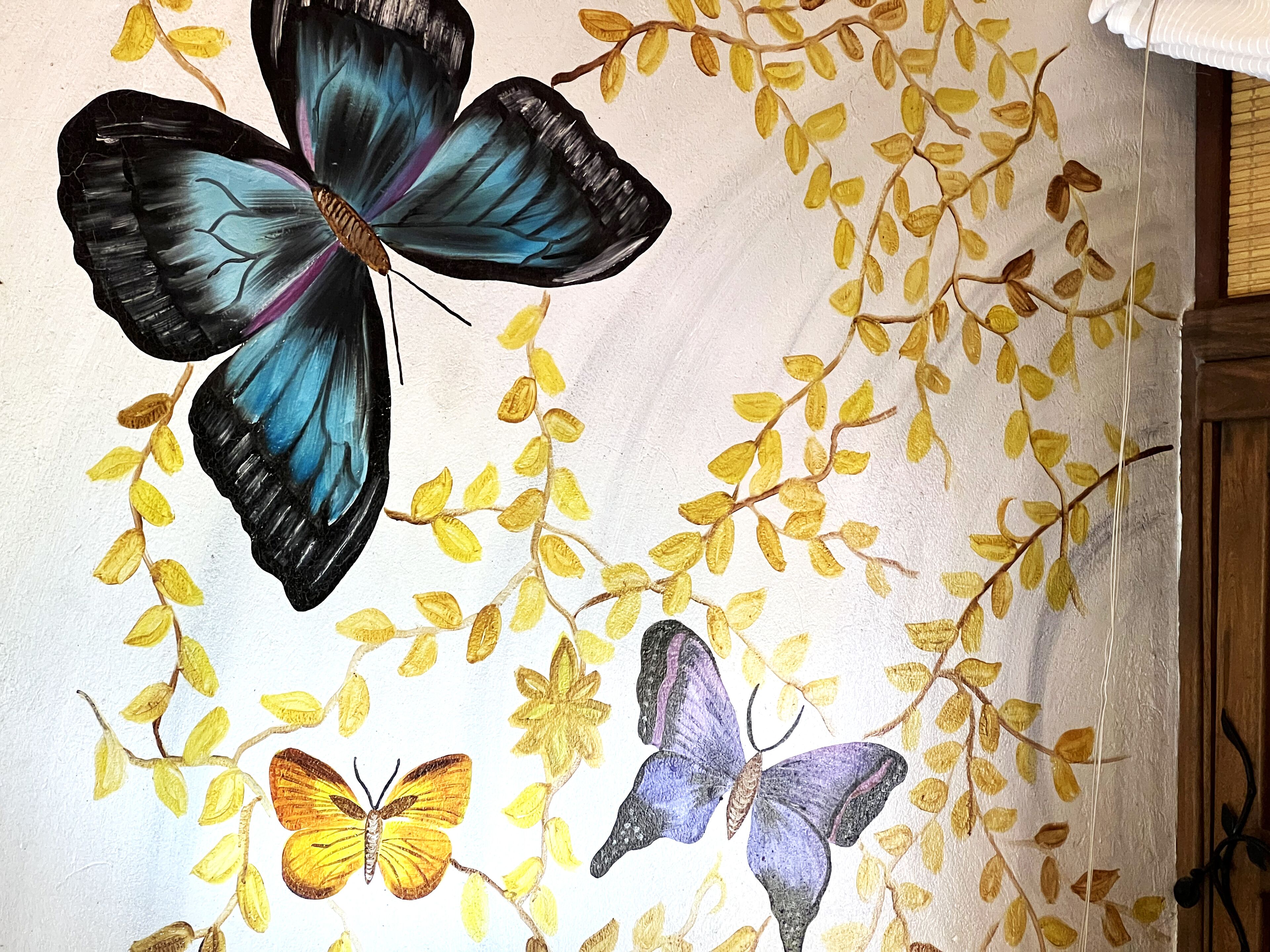 A wall with a painted mural of butterflies and leaves.