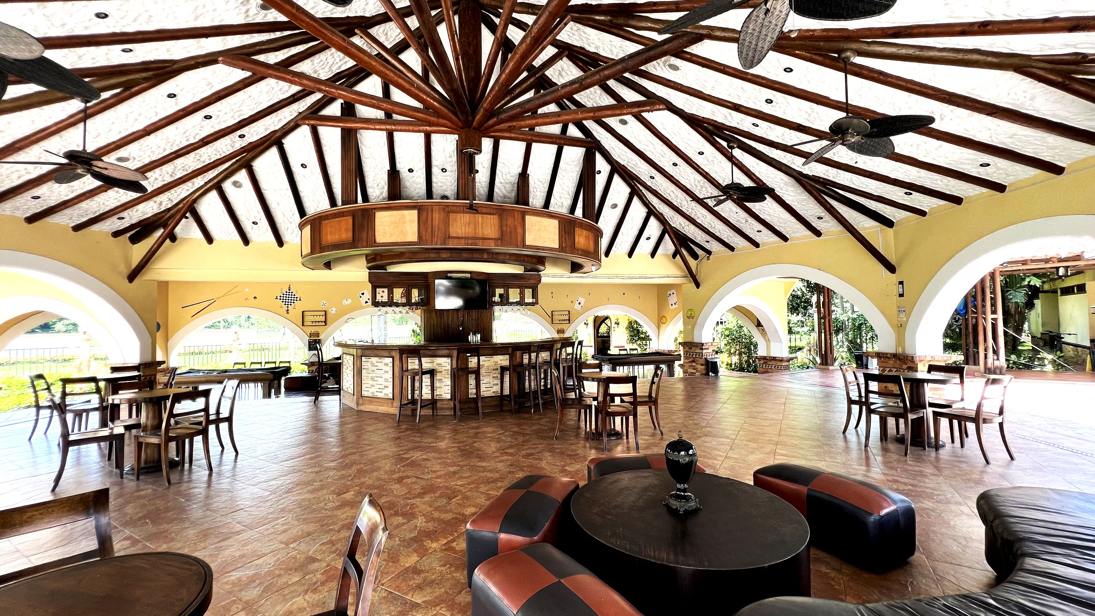 Un espacio interior amplio con un alto techo de madera, varios arreglos de asientos y una zona de bar central.