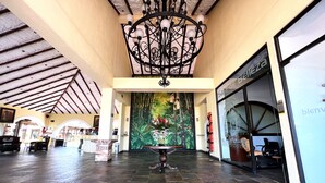 Un vestíbulo espacioso con suelo de baldosas, una lámpara decorativa, un mural grande y un mostrador de recepción.