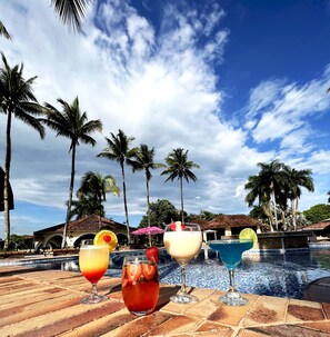 A poolside area with three drinks, palm trees, and a tiled pool. - Tequendama Hotel Campestre Villavicencio (Villavicencio)