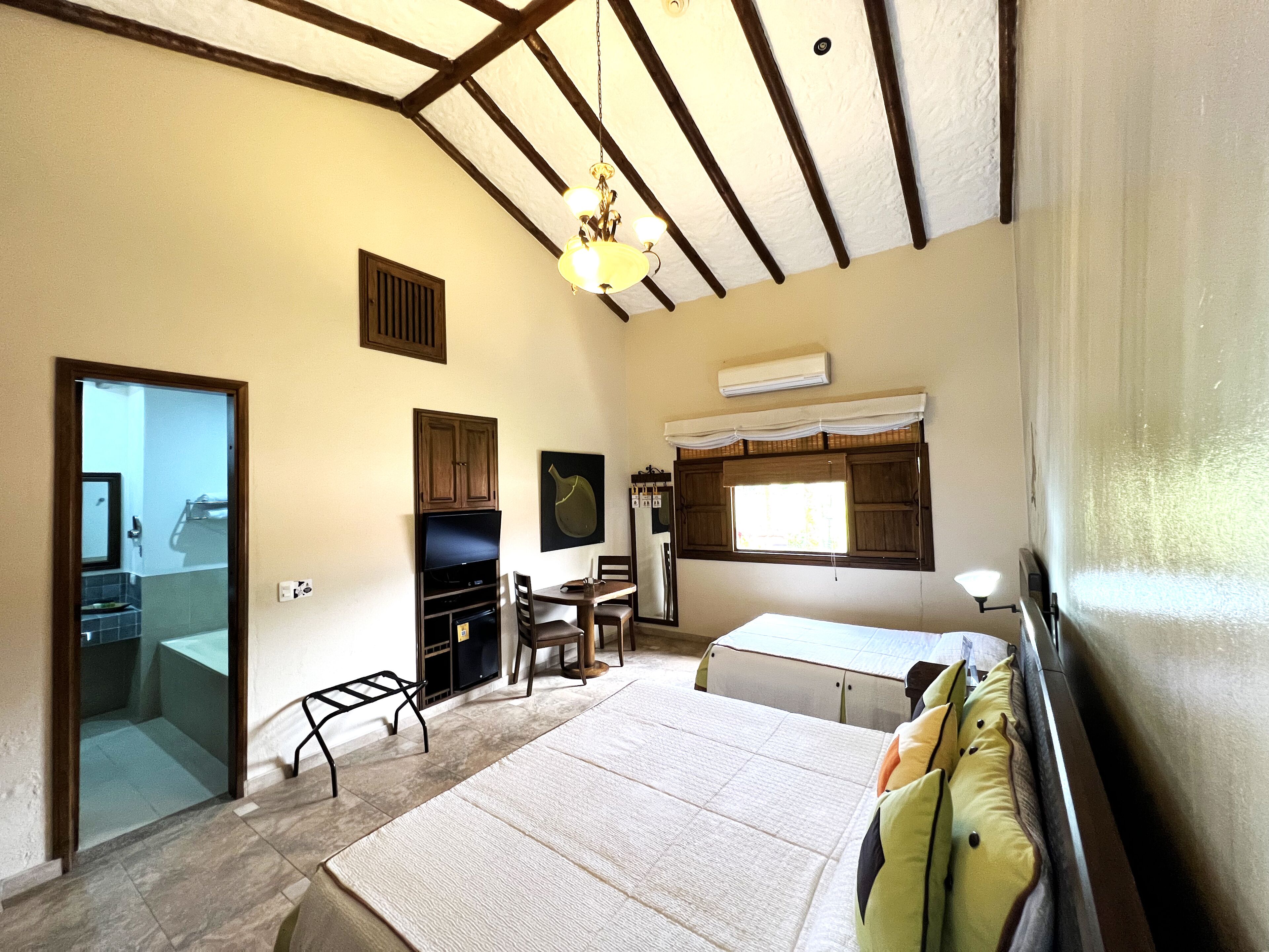 Una habitación con cama, escritorio, silla, televisor y ventana con cortinas.