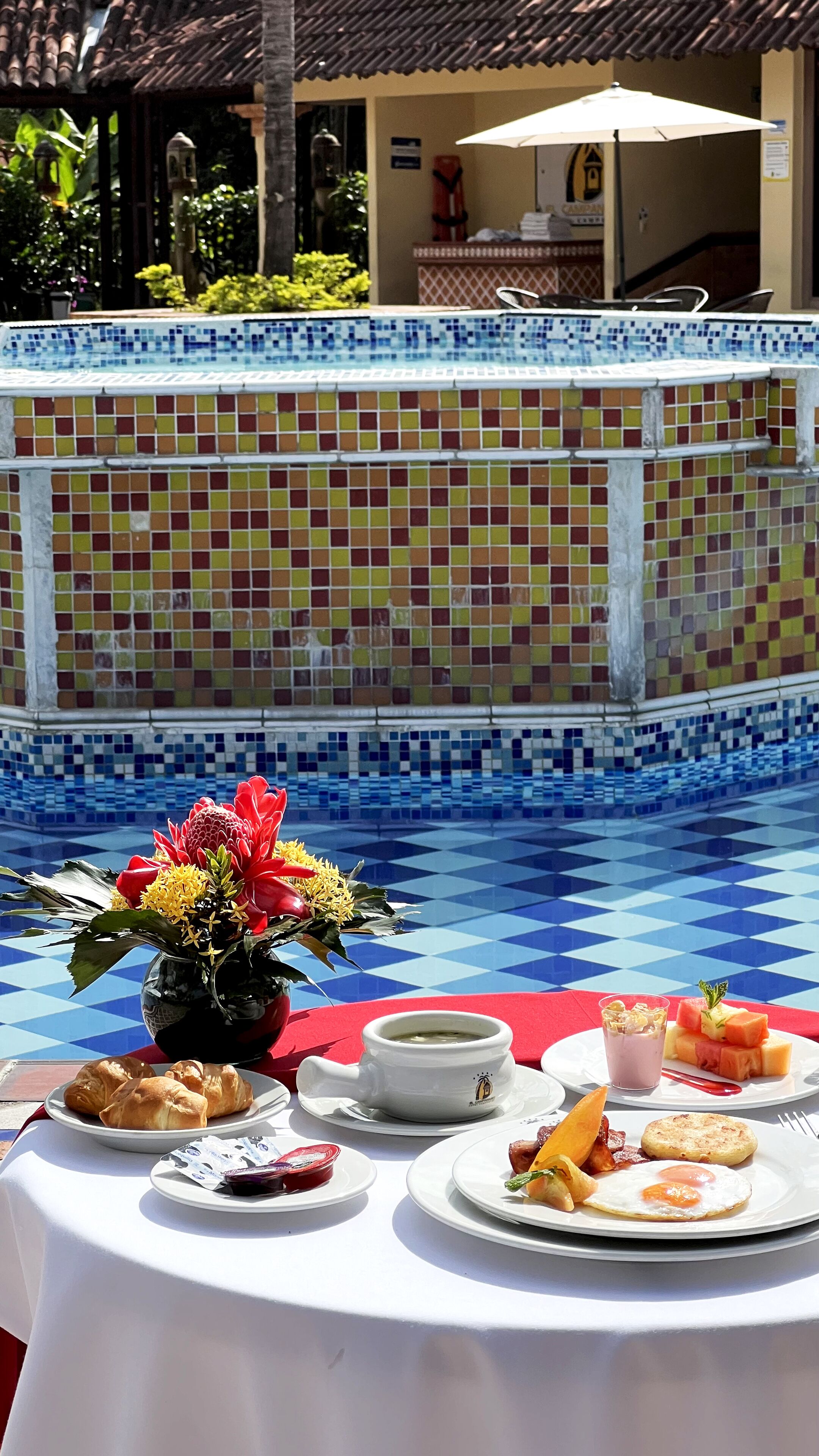 A poolside table with a variety of food items and a flower arrangement.