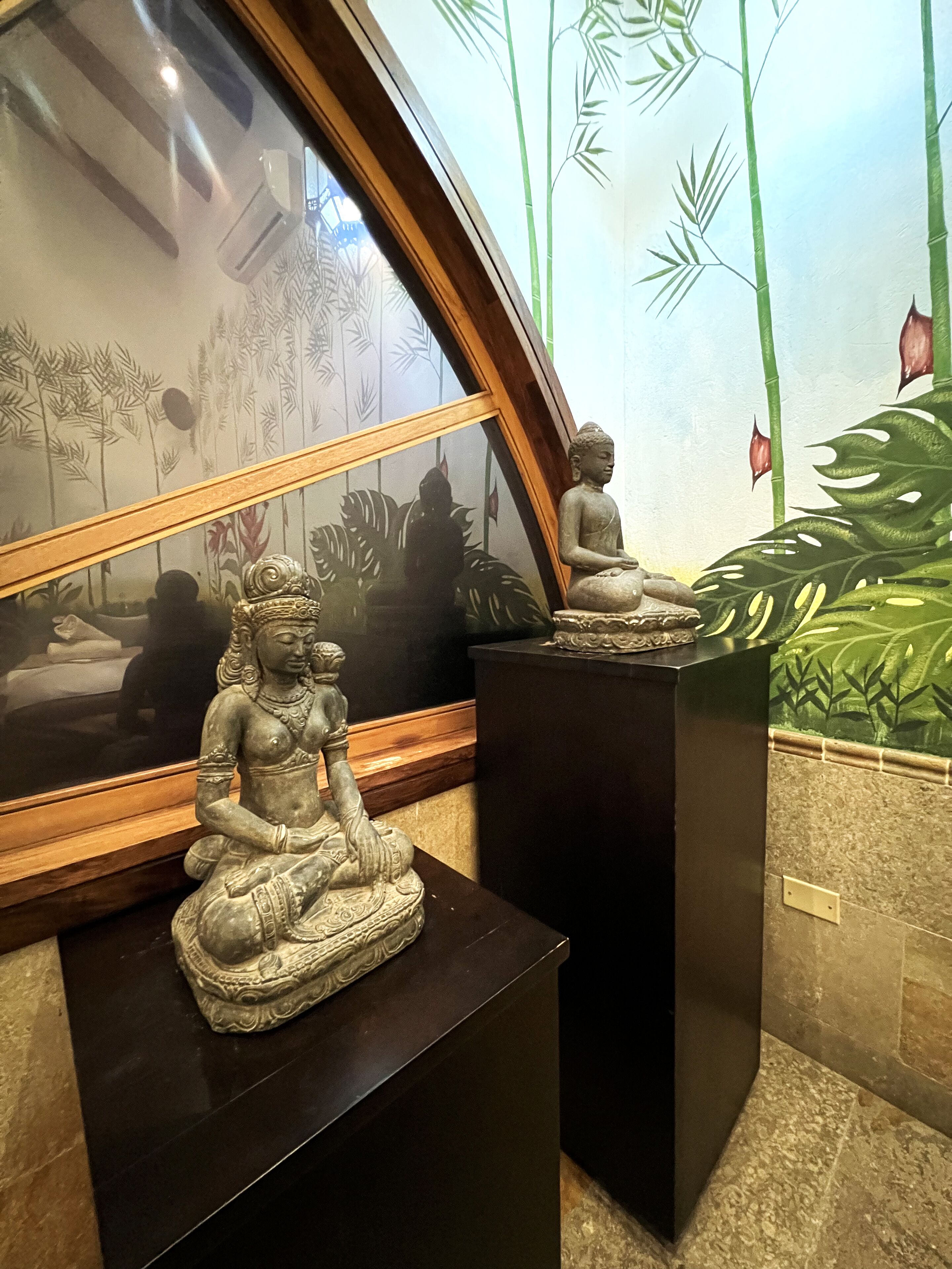 A statue of a seated figure on a pedestal, a framed artwork with a bamboo motif, and a wall with a bamboo pattern.