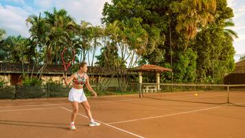 Un court de tennis avec un filet, entouré de palmiers et agrémenté d’un petit pavillon.