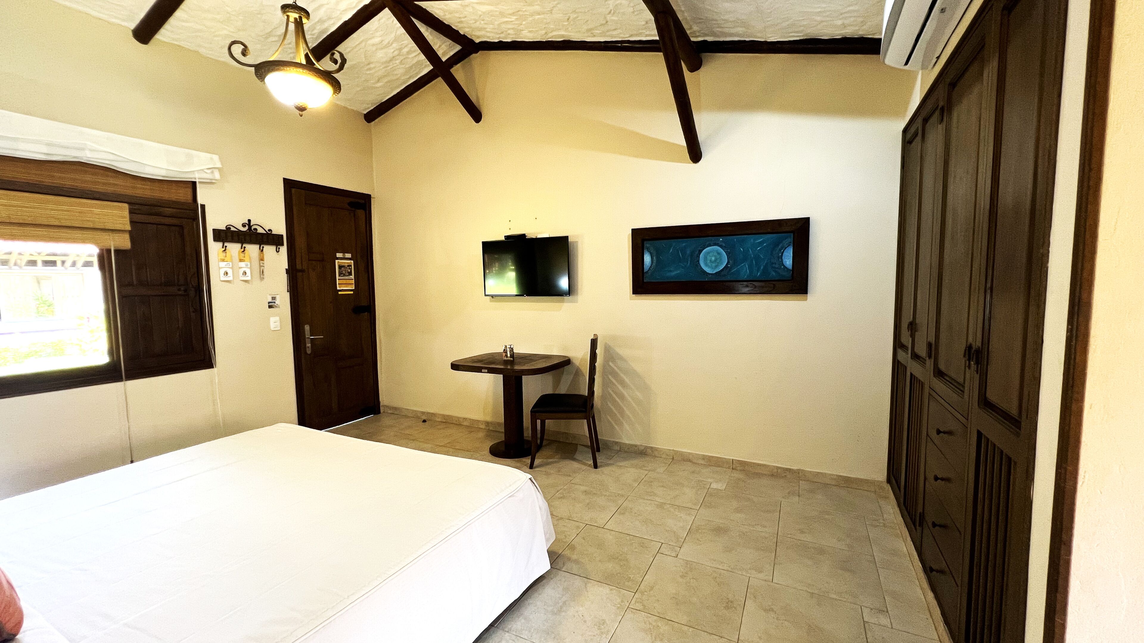 Una habitación de hotel con cama, una mesita, una silla, televisión y armario.