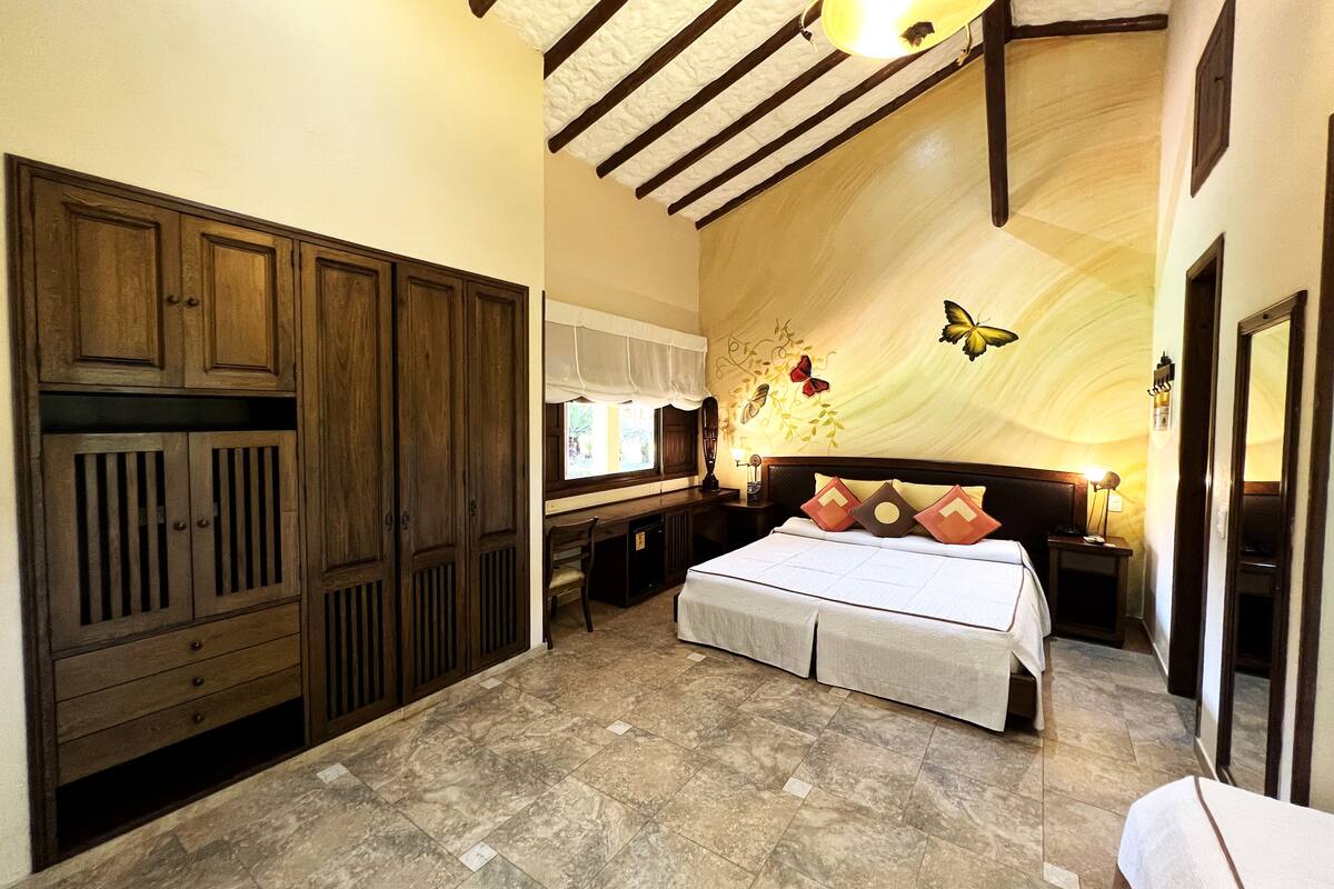 A bedroom with a large bed, wooden wardrobe, and a decorative ceiling.