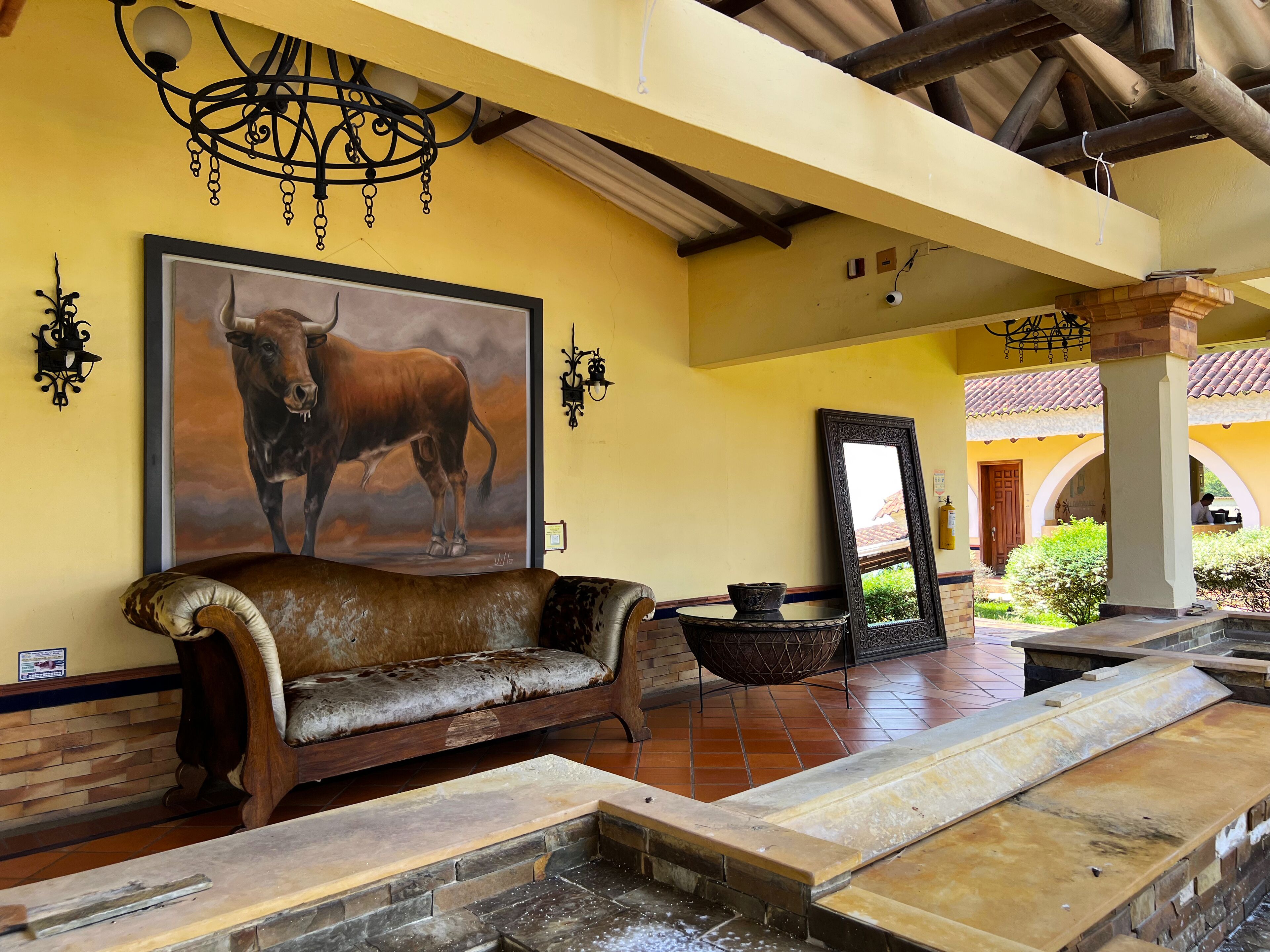 A yellow-walled room with a bull painting, a sofa, a mirror, and a small fountain.